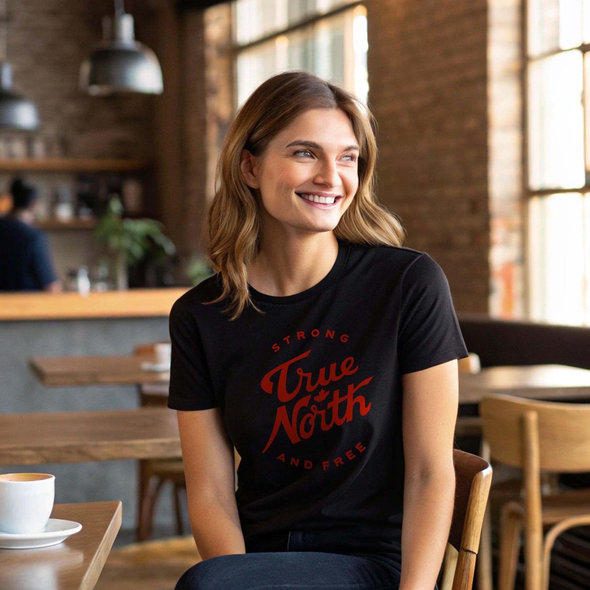 Woman wearing a black t-shirt with 'True North Strong and Free' text in a coffee shop.
