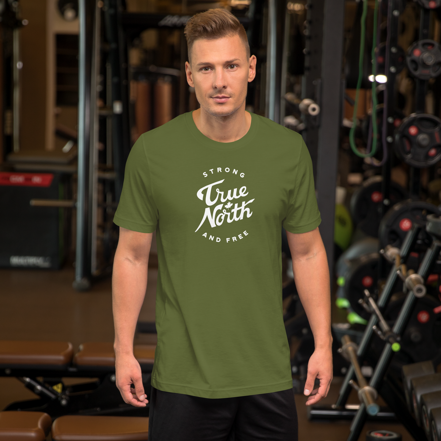 Man wearing an olive green t-shirt with 'True North Strong and Free' text in a gym setting